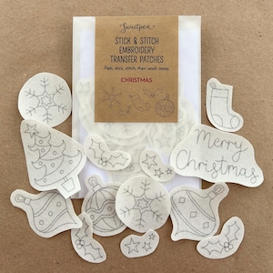 May include: A set of 14 white iron-on embroidery transfer patches featuring Christmas designs. The designs include a Christmas tree, baubles, snowflakes, stars, holly, and the words "Merry Christmas".