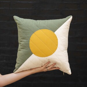 May include: A green and white quilted pillow with a large yellow circle in the center. The circle has a quilted pattern.