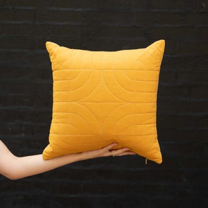 May include: A yellow quilted pillow with a geometric pattern. The pillow is made of a soft, plush fabric and has a zipper closure.