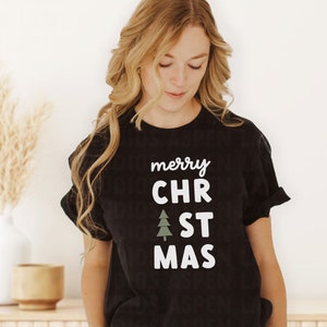 May include: Black t-shirt with white text that reads "merry CHR". A green stylized Christmas tree graphic is between the words "CHR" and "ST". The text continues with "ST MAS".