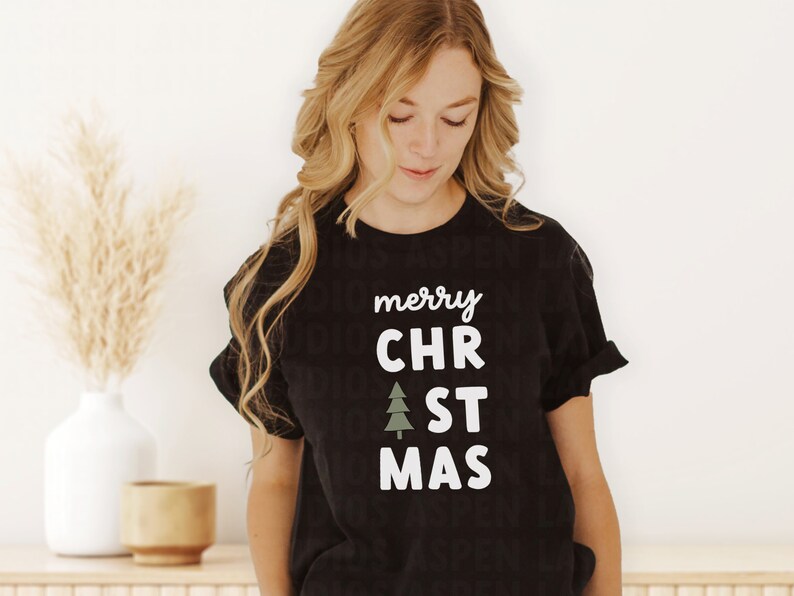 May include: Black t-shirt with white text that reads "merry CHR". A green stylized Christmas tree graphic is between the words "CHR" and "ST". The text continues with "ST MAS".