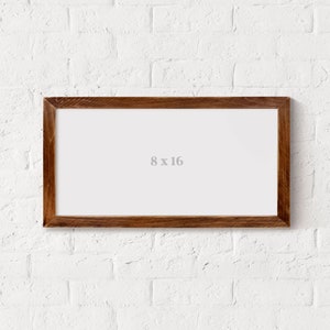May include: A brown wooden picture frame with a white mount and the text "8 x 16" printed in the centre. The frame is hanging on a white brick wall.