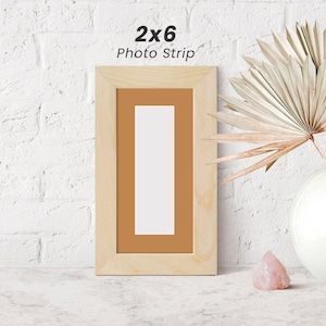 May include: A natural wood picture frame with a 2x6 photo strip. The frame has a light brown mat and a light brown wood finish.