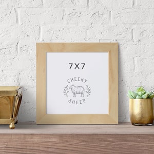 May include: A natural wood picture frame with a white mat and a print of a sheep with the text "7x7 Cheeky Sheep".