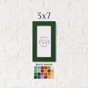 May include: A rectangular green picture frame, 7.6 cm by 17.8 cm, with the text "3x7" above it. The frame contains a white background with a sheep illustration and the words "Cheeky Sheep". Below the frame is a color palette labeled "Rustic Painted".