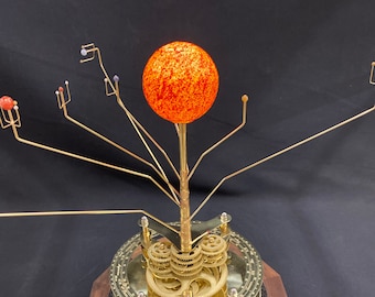 May include: A brass and wood solar system model with a red and orange sun, gold gears, and a wooden base.