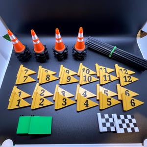 May include: A set of orange traffic cones, yellow flags with numbers 1-12, a green flag, and a checkered flag. The cones are stacked on black bases. The flags are made of yellow cardboard with black numbers.