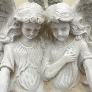 May include: Two white angel figurines with wings, one with long hair and the other with short hair, both with a serene expression.