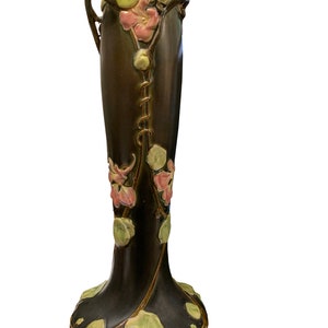 May include: A tall, dark brown ceramic vase with a floral design. The vase has a slender neck and a wide base. The flowers are in shades of pink, green, and brown.