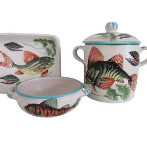 May include: A set of three ceramic dishes featuring a hand-painted fish design. The dishes are white with blue trim and feature a green, orange, and black fish with a white background.