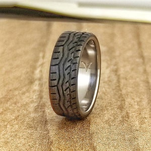 May include: A black and silver ring with a tire tread design. The ring is made of titanium and features a black rubber inlay.