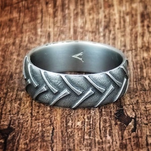 May include: A silver ring with a tire tread design. The ring is made of metal and has a brushed finish.