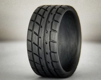 May include: A black rubber tire with a tread pattern designed for racing. The tire is round and has a smooth, black surface.
