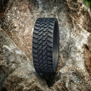 May include: A black rubber ring with a tire tread pattern. The ring is sitting on a rock.