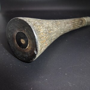May include: A close-up of a wooden club with a dark, circular end. The club has a textured, light brown handle and a dark brown, circular end with a central hole. The club appears to be handmade.