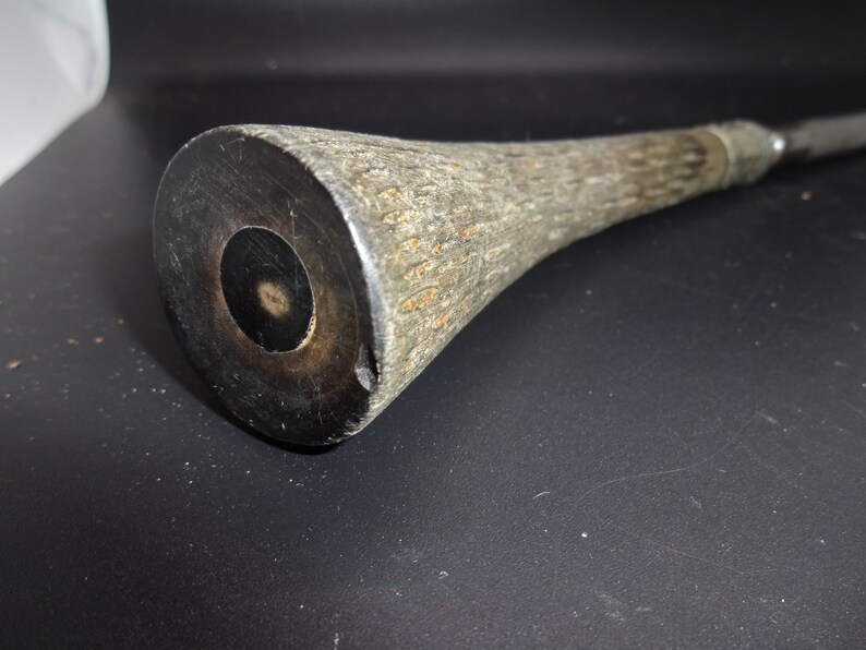 May include: A close-up of a wooden club with a dark, circular end. The club has a textured, light brown handle and a dark brown, circular end with a central hole. The club appears to be handmade.