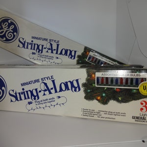 May include: Two boxes of General Electric miniature style String-A-Long Christmas lights. The boxes are white with blue lettering and a blue GE logo. The top box shows a string of lights with assorted color bulbs. The bottom box shows a string of lights with assorted color bulbs and a Christmas tree with lights. The bottom box also has a UL safety certification label and says "35 Light Set" and "General Electric Indoor/Outdoor".