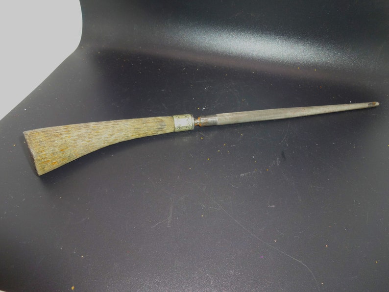 May include: A steel knife sharpener with a light-colored, textured handle. The handle is curved and attached to a long, tapered steel rod. A silver band connects the handle to the steel rod. The sharpener is designed for sharpening knives.