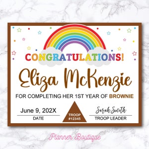 Puede incluir: Un certificado con temática de arcoíris con el texto "CONGRATULATIONS!" y "Eliza McKenzie" por completar su primer año de Brownie Girl Scouts. El certificado incluye la fecha "June 9, 202X", el número de tropa "#12345" y el nombre del líder de la tropa "Sarah Smith". El certificado está decorado con estrellas y un arcoíris.