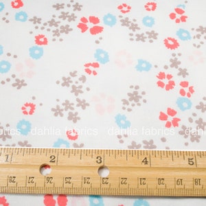May include: White fabric with a repeating pattern of small pink, blue, and gray flowers. A wooden ruler is placed on top of the fabric, with the numbers 1 through 6 visible.