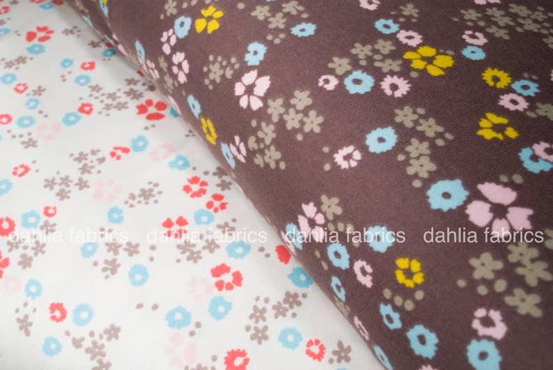 May include: Two fabric swatches with floral patterns. The top swatch is brown with a white, pink, and yellow floral pattern. The bottom swatch is white with a light blue, pink, and red floral pattern.