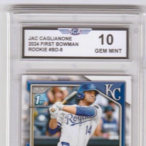 May include: A baseball trading card of Jac Caglianone in a protective case. The card features a photo of the player in a Kansas City Royals uniform. The card is graded a 10 GEM MINT by SCA. Text on the card includes "2024 First Bowman Rookie #BD-8".