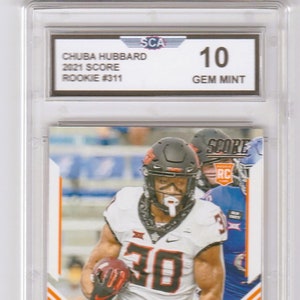 May include: A graded sports card featuring a football player in a white jersey with black and red accents. The card is graded 10, Gem Mint, by the Sportscard Guaranty Corporation (SCG). The card features the player's name, "Chuba Hubbard", and the team name, "Cowboys".