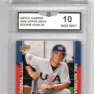 May include: A baseball card featuring Bryce Harper, a catcher/outfielder for the 18U National Team. The card is graded GEM MINT 10 by SCA. The card is from the 2009 Upper Deck Rookie set.