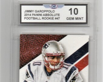 May include: A graded sports card featuring a football player in a white jersey with a red, white, and blue helmet. The card is graded 10 Gem Mint by the Sports Card Authenticator (SCA). The card features the text "HOGG HEAVEN" and "JIMMY GAROPPOLO".