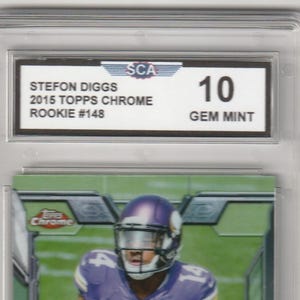 May include: A graded trading card featuring Stefon Diggs in a purple and white football uniform. The card is from the 2015 Topps Chrome Rookie series, graded a 10 Gem Mint. The card is encased in a protective holder with the text "STEFON DIGGS" and "VIKINGS".