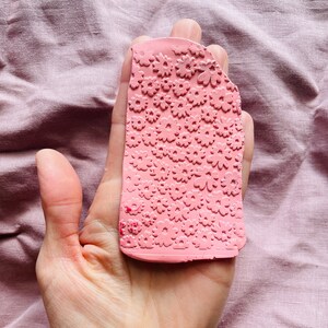 May include: A pink polymer clay stamp with a repeating pattern of small white flowers.