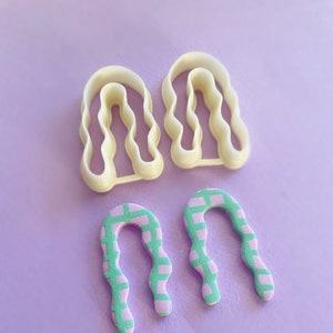 Pode incluir: Dois cortadores de biscoitos de plástico branco em forma de arcos ondulados e dois arcos com padrões rosa e verde.