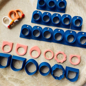 May include: A set of blue and pink silicone ring molds for making jewelry. The molds are arranged in rows on a beige plate. The molds are labeled with letters from A to Z.