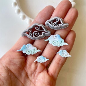 May include: Five cloud-shaped cookie cutters, two are grey and three are blue and white with a swirl design.