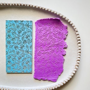 Puede incluir: Un rodillo de silicona azul y morado con un patrón de hojas. El rodillo se utiliza para crear patrones decorativos en fondant o arcilla.