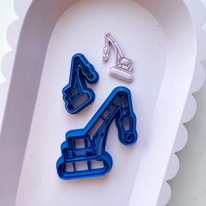 May include: Three cookie cutters in the shape of construction cranes. Two are blue and one is pink.