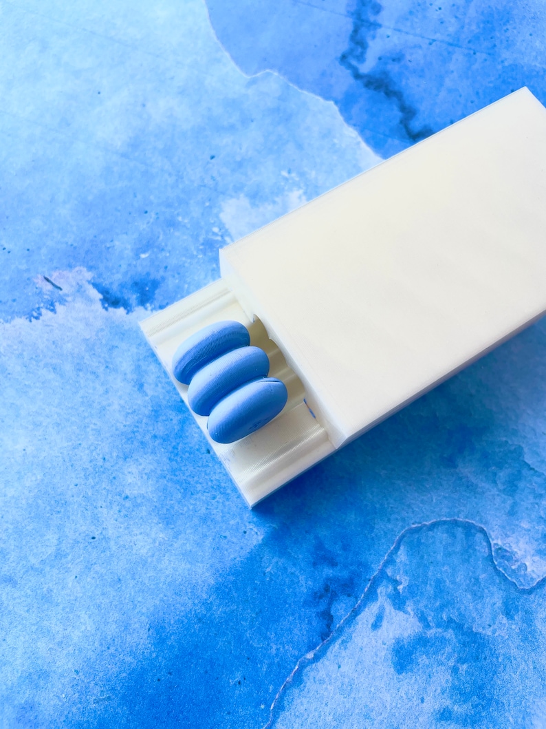 May include: A white plastic dispenser with three blue round pills inside.