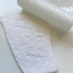 Puede incluir: Primer plano de un objeto rectangular blanco y texturizado con un objeto blanco enrollado encima. Los objetos parecen estar hechos de un material poroso, posiblemente para manualidades o proyectos artísticos.