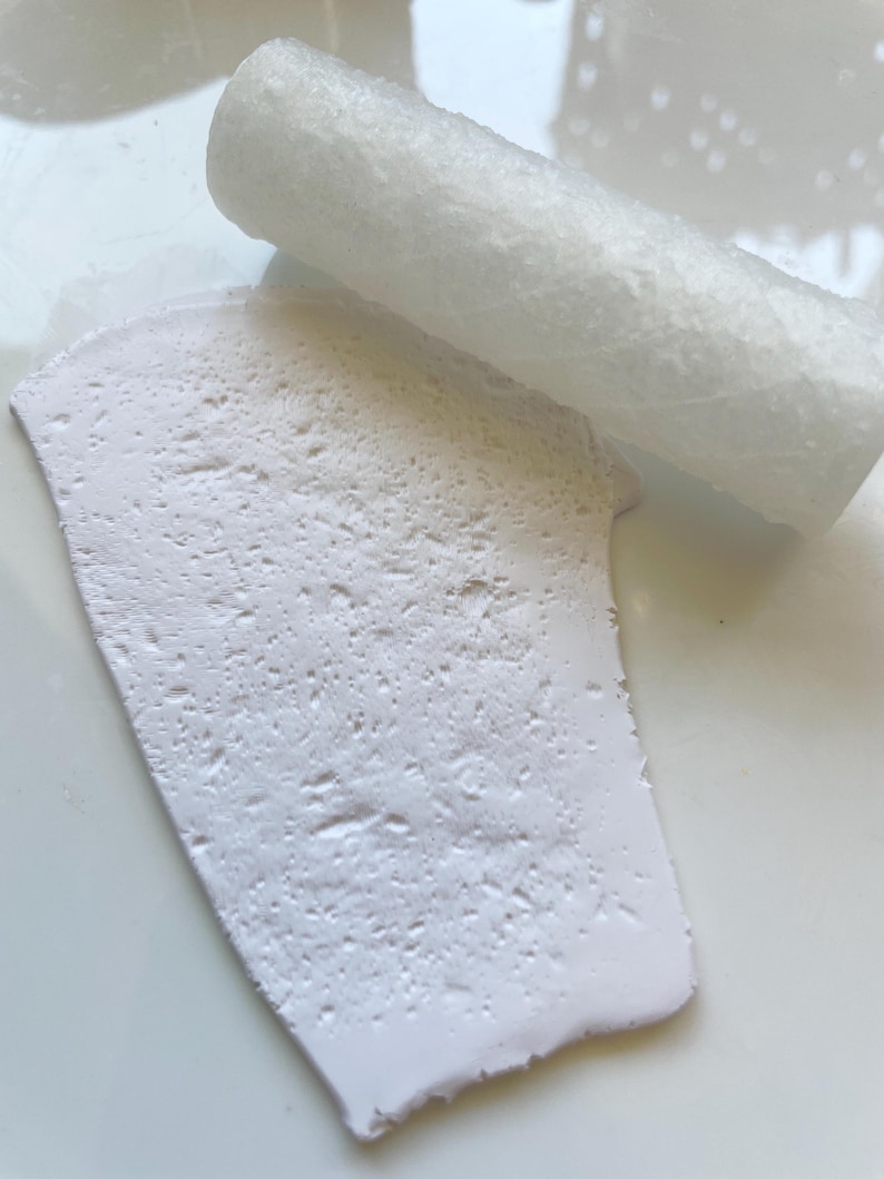 May include: A close-up of a white, textured, rectangular object with a rolled-up white object on top. The objects appear to be made of a porous material, possibly for crafting or art projects.