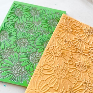 May include: Two silicone baking mats with a daisy pattern. One mat is green and the other is yellow.