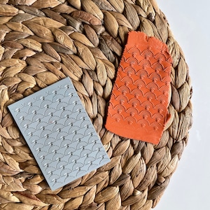 May include: Two silicone embossing mats with a fan-shaped pattern. One mat is gray and the other is orange.