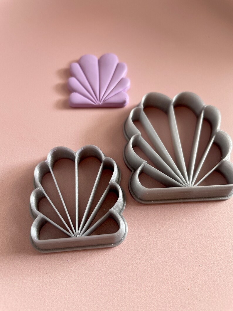 Photo of an Art Deco clay cutter in 2 different sizes, next to a sample of polymer clay earring cut with the same mould. The shape resembles a seashell.