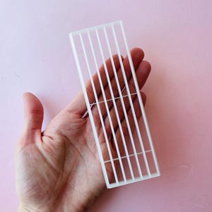Könnte beinhalten: Weißes Plastik-Kuchendekorationswerkzeug mit einem Gittermuster. Das Werkzeug ist etwa 15 cm lang und 5 cm breit.