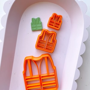 May include: Three orange plastic cookie cutters shaped like life vests. The smallest cutter is green.