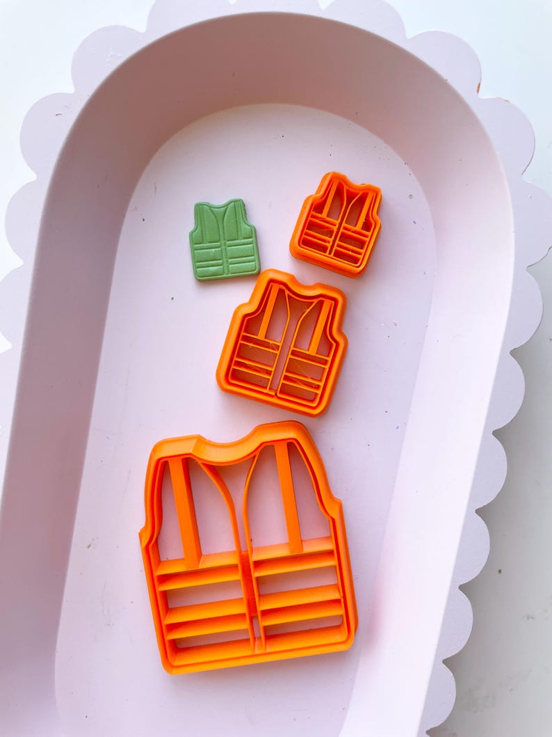 May include: Three orange plastic cookie cutters shaped like life vests. The smallest cutter is green.