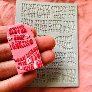 May include: Pink silicone mold with the text "Never Stop Making" and "Grow Through What You Throw" in a retro font. The mold is being held in a hand.