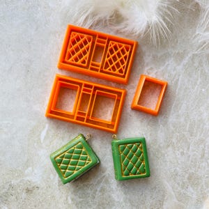 May include: Two green book-shaped polymer clay charms with gold accents and a diamond pattern. Four orange plastic moulds for making the charms are also shown.
