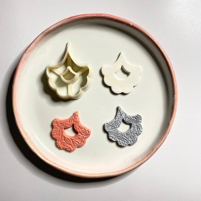 May include: Four polymer clay flower shapes, two are white and untextured, one is pink with a leaf pattern, and one is gray with a leaf pattern.