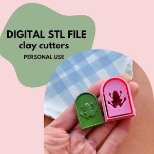 Peut inclure: Deux découpoirs à argile en forme de grenouille, un vert et un rose, tenus dans une main. Le texte sur l'image indique "DIGITAL STL FILE clay cutters PERSONAL USE".