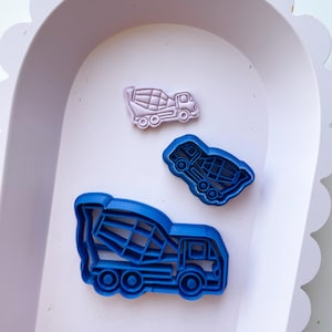 Puede incluir: Tres cortadores de galletas con forma de camión mezclador de cemento. El cortador más grande es azul, el mediano es azul y el más pequeño es rosa.